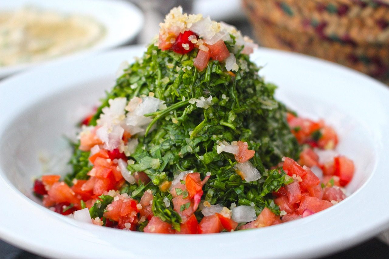 miska zielonego tabbouleh z natki z bulgurem i pomidorami obok fattoush z grzankami