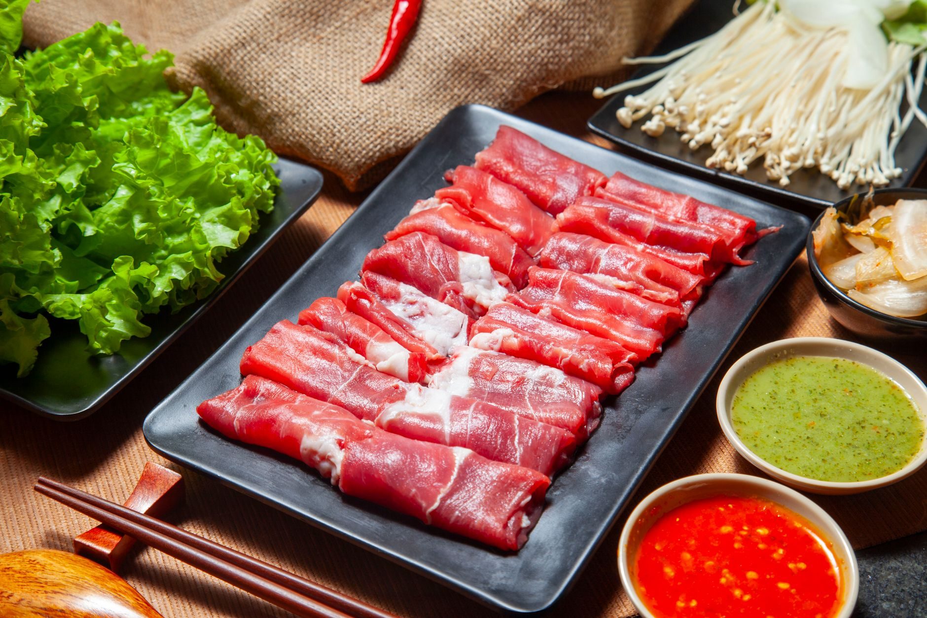 dzielony kociołek hot pot czerwono-biały otoczony talerzami dodatków