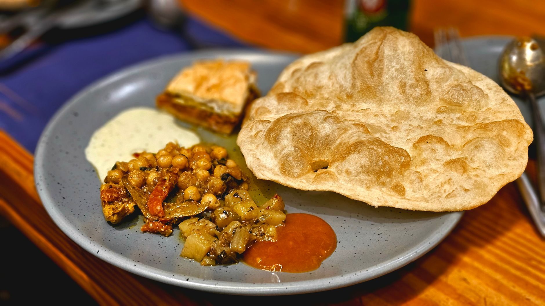 nadmuchany złoty chleb bhatura obok miski ciemnej ciecierzycy