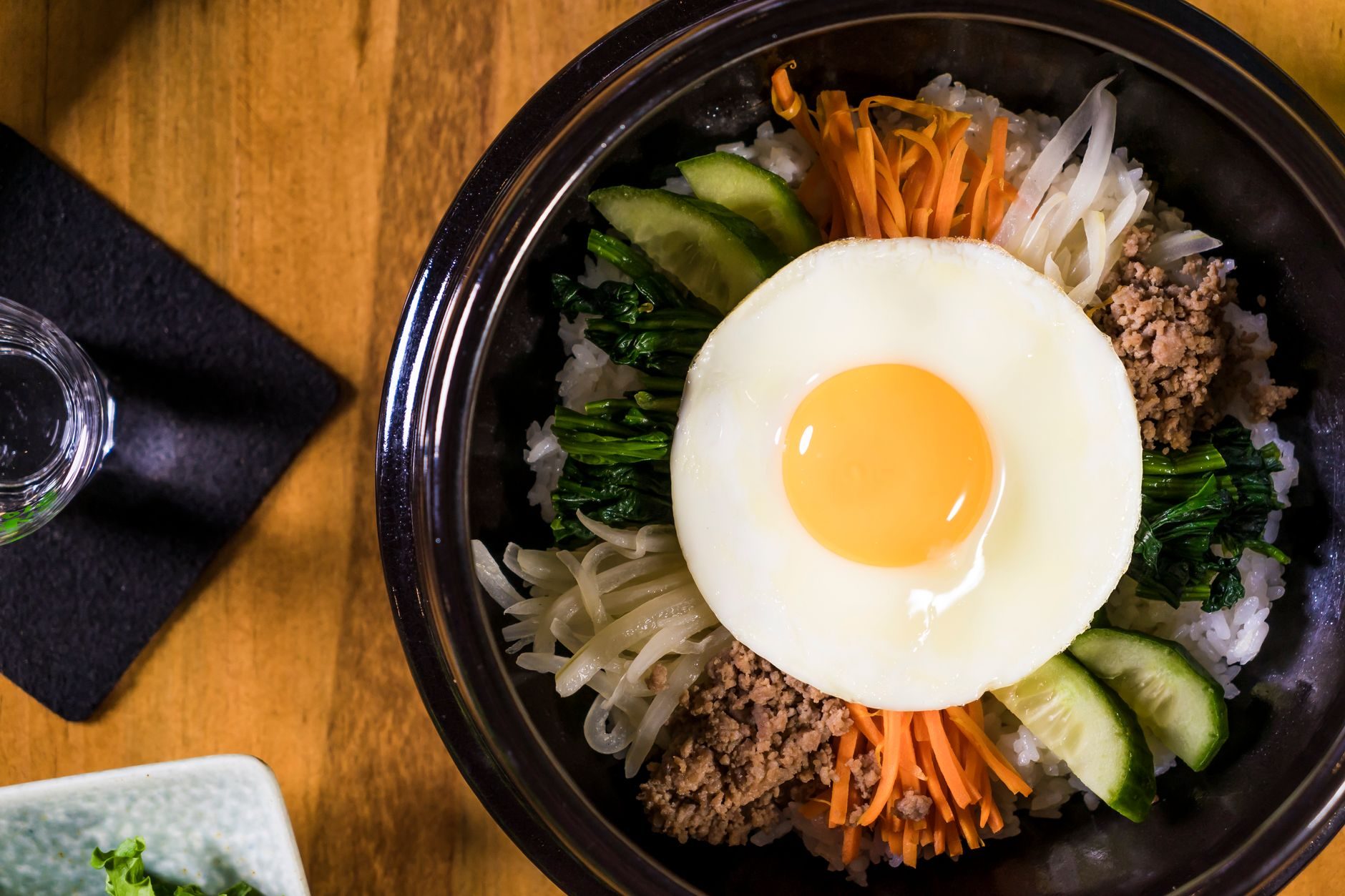 kamienna miska bibimbap z jajkiem i kolorowymi warzywami przed wymieszaniem