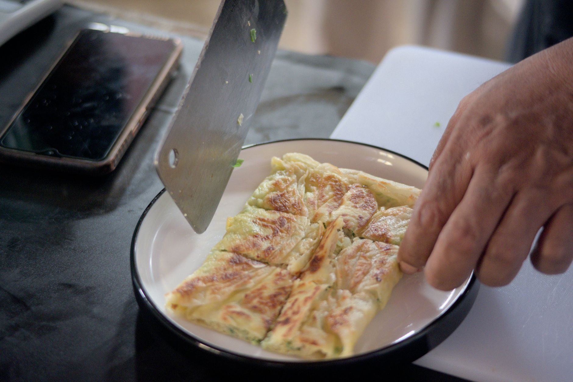 kucharz rozciąga w powietrzu cienkie ciasto na roti canai przy rozgrzanej płycie
