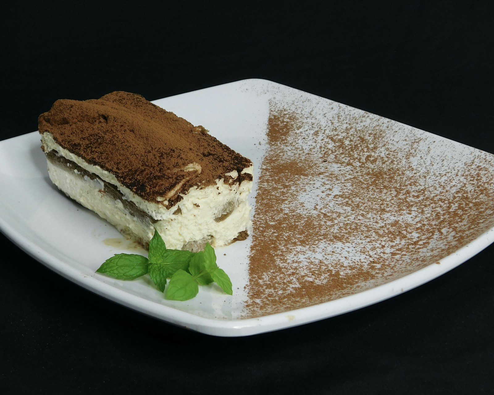 kostka tiramisu z widocznymi warstwami, gęsto oprószona kakao